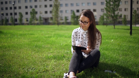 Beautiful Student In Glasses With Digital Tablet Sitting On The Grass