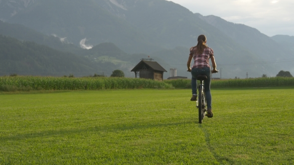 Beautiful Woman Cycles Through Green Alpine Meadow