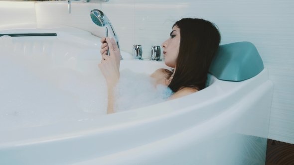 Brunette Girl Taking Bath Full Of Foam. Tap In Smartphone. Relax. Resting. alt