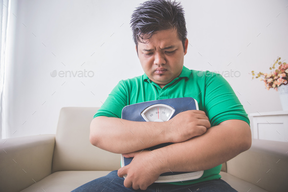 sad obese man holding a weight scale, thinking about his weight