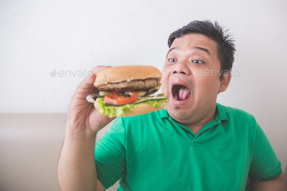 Overweight man eating hamburger at home