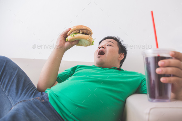 lazy obese person eats junk food while laying on a couch
