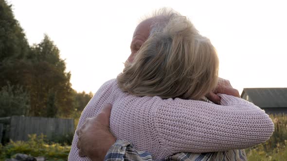 Elderly Couple In Love Hugs In Park Against Of Sunlight At Sunset At Summer Fall alt