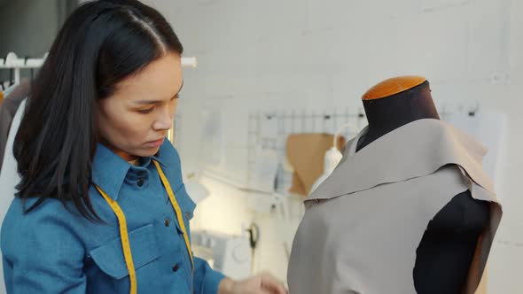 Pensive Young Woman Sewing Fashionable Clothing on Tailor's Dummy Working Alone in Studio alt