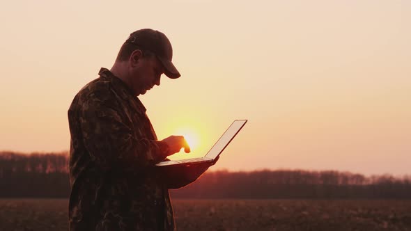 Serious Farmer Working with Laptop in the Field at Sunset alt