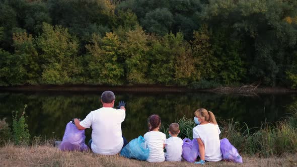 A family of volunteers after collecting garbage sit on the river Bank and watch and admire nature. 