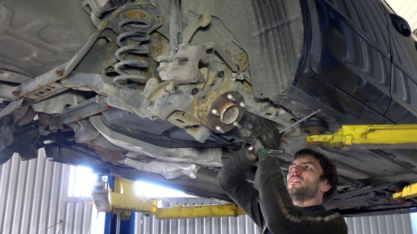 Skilled Mechanic Removing Worn Car Parts in Garage Under Automobile.