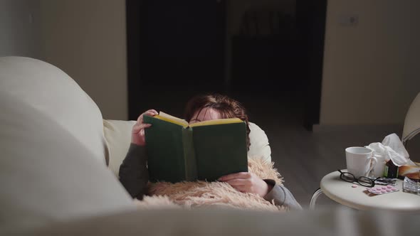 Sick Brunette Woman Lies on the Sofa and Reads a Book in the Evening