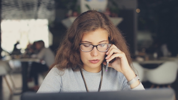 Woman Talking On The Phone In a Cafe. Laptop On Table alt