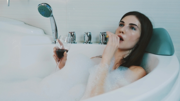 Girl With Red Wine Glass In Bath Full Of Foam. Smoking Electronic Cigarette.