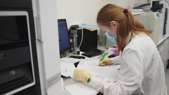 Woman Wearing Protective Mask and Medical Uniform is Writting the Data to the Notebook