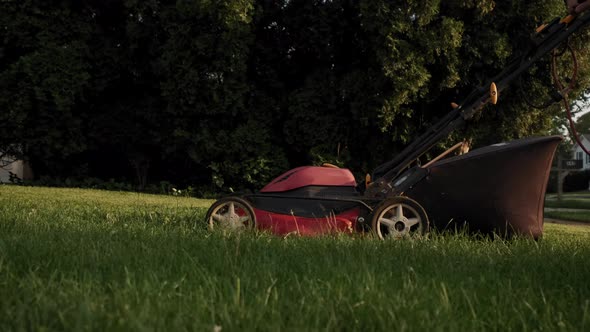 Close Up of Man Cut Grass with Lawn Mower in House Yard Near Swing in Playground alt