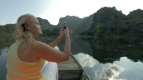 Female Tourist Taking Photos With Cell During Boat In Trang An, Vietnam alt