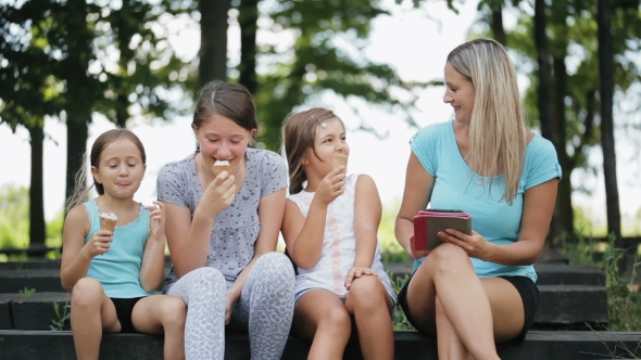 Attractive Mom With Three Daughters In a Park. Woman Enjoys The Tablet. alt