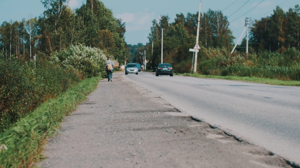 Man Walk Along The Road In Countryside With Cardboard Plate. Hitchhiking. Cars