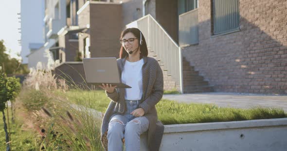 Good-looking Woman Using Computer Laptop with Headset Talking on Video Call Looking at Camera alt