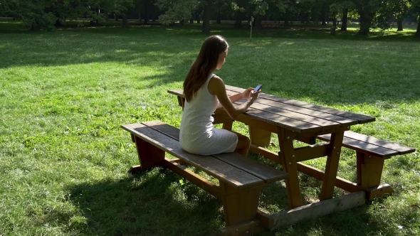 Woman Texting And Browsing On Bench In Park