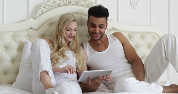Couple Lying Bed Using Tablet Computer, Mix Race Man Woman Smile Morning Bedroom alt