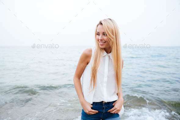 Cheerful woman with long blonde hair standing on the beach - Stock Photo - Images
