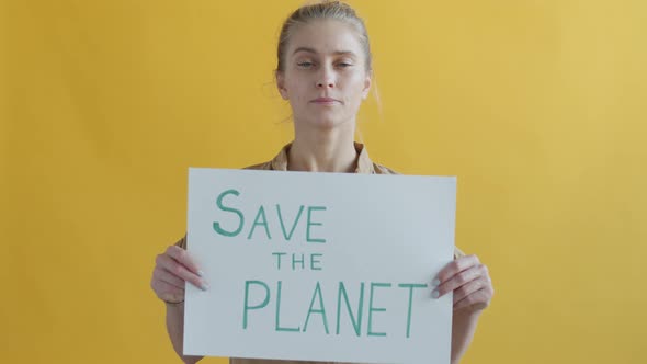 Portrait of Serious Woman Activist Holding Save Planet Banner on Yellow Background alt