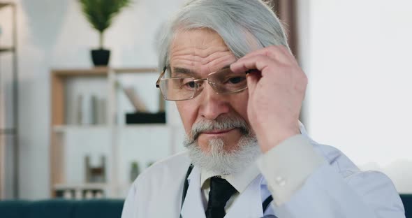 Doctor Putting on His Eyeglasses and Looking Into Camera with Trustful Face Expression Indoors alt
