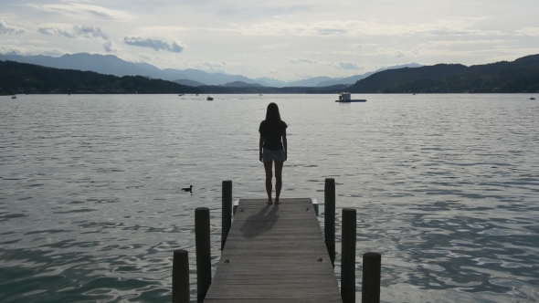 Pensive Woman Stands On Dock Of Clear Lake