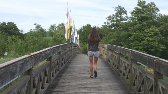 Woman Walks Over The Wooden Bridge With Flags