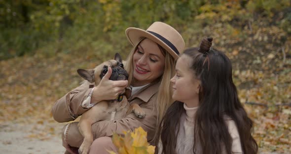 Stylish Mother and Daughter Playing with Pet Sitting in Autumn Park alt