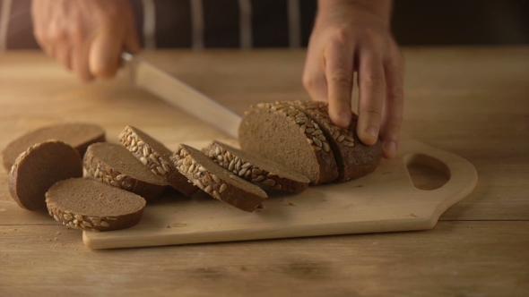 Hands Cutting Bread With Knife On Rustic Wooden Table