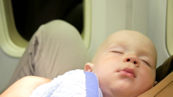Mom And Baby Are Resting On The Plane During The Flight. Night Flight Over The Ocean. The Child's