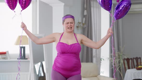 Medium Shot of Funny Obese Woman Raising Balloons Imitating Weight Lifting Looking at Camera alt
