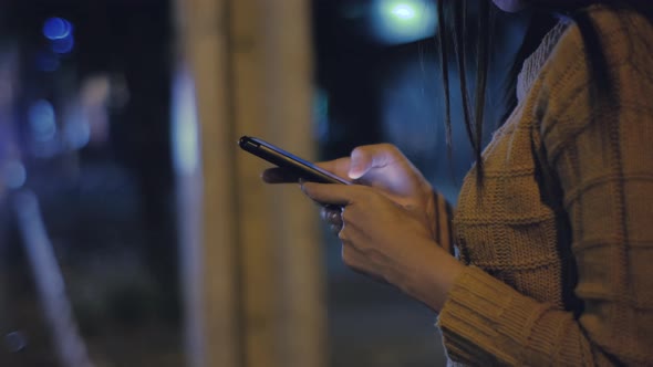 Female hands using smartphone at night on city shopping street
