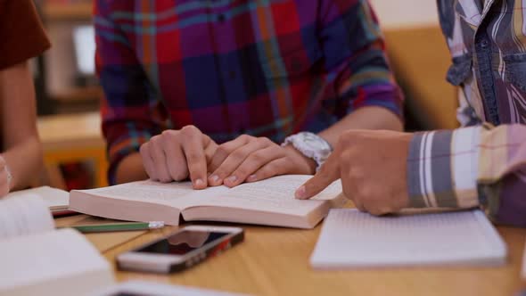 Close Up Footage of Three Friends Sitting at Library Reading Book and Underlining with Pencil in alt