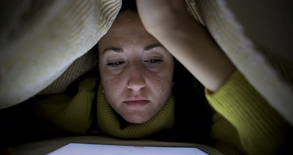 Woman at home staying on the bed under the blanket and reading studying on di