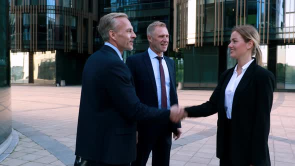 Two Businessmen Meet a Businesswoman and Shake Hands with Her Then Chat Together. Modern Office