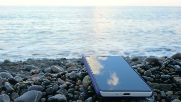 The Mobile Phone Is About The Pebble Beach Of The Ocean. Calm Waves Beating Against The Shore
