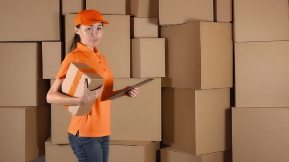 Beautiful Female Courier In Orange Uniform Delivering a Parcel Against Carton Stacks Backround alt