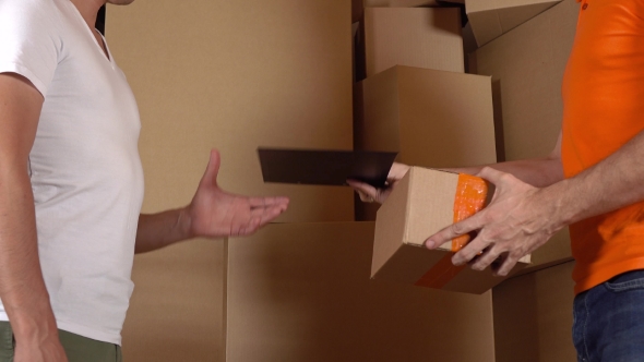 Store Assistant In Orange Uniform Giving a Box To a Customer. Cartons Background,  Studio Shot alt