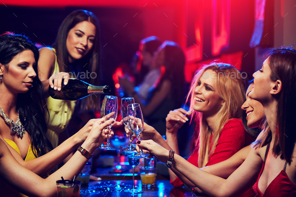 Smiling girl in the club poured champagne to her friends