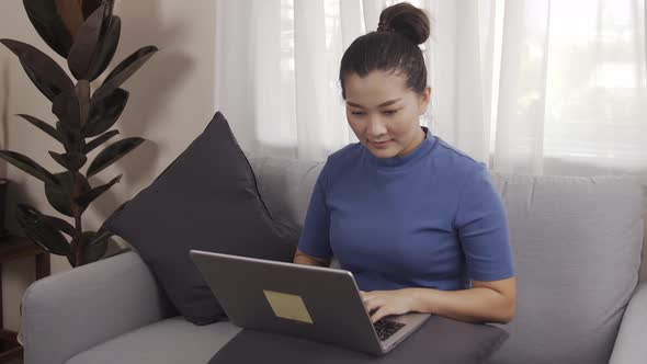 New normal businesswoman work from home by laptop sitting on the sofa happily alt