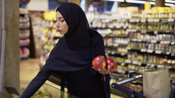 Muslim Woman Shopping for Groceries Taking Red Apples From the Fruit Aisle alt