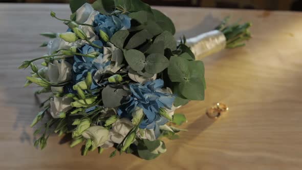 Wedding Rings Lie Near Beautiful Wedding Bouquet on the Wooden Table alt