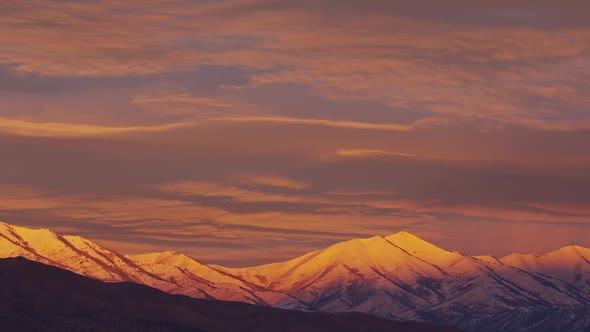 Sun lighting up the clouds and snow capped mountains at sunrise alt