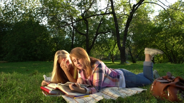 Happy Teenage Girls Reading a Book Outdoors.