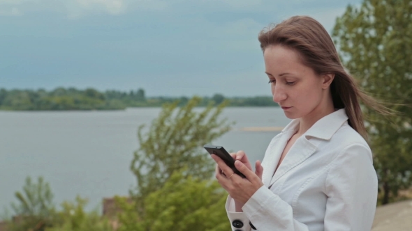 Beautiful Girl Standing On The Embankment Of The River With The Phone