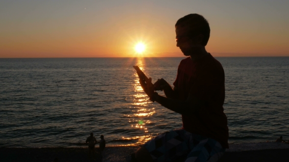 Silhouette Man With Digital Tablet In Hands At Sunset Beach alt