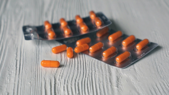 Hand Folds Pills in Orange Capsule Form on a Table