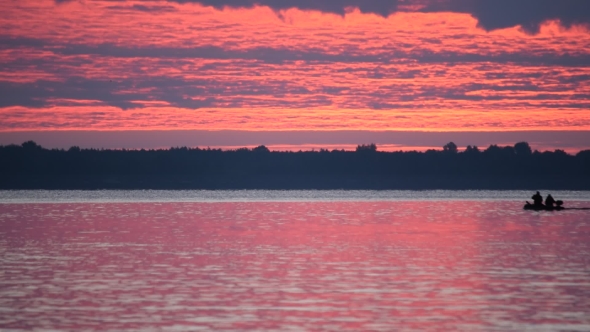 Silhouettes Of Two Men In a Boat At Dawn On Water