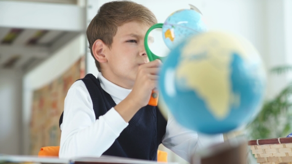 The Boy Looks At The Globe Using a Magnifying Glass.