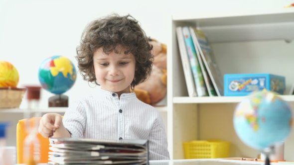 Child And Book. Cute Boy With Black Curly Hair Opens The Book